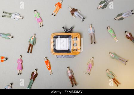 Figurine persone intorno retro syled piccolo televisore su sfondo giallo Foto Stock