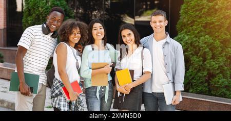 Gruppo multietnico di studenti che si trovano all'aperto nel campus scolastico con libri di lavoro Foto Stock