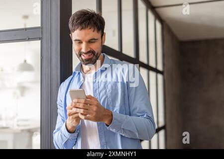 Uomo sorridente mentre utilizza lo smartphone in un ambiente ufficio moderno Foto Stock