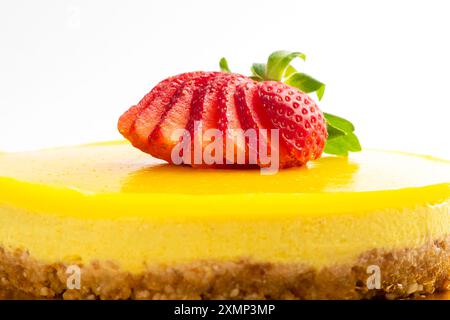 Una vivace cheesecake di mango con fragole a fette su sfondo bianco. Delizioso dessert da gustare. Primo piano Foto Stock