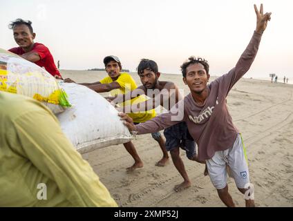 Uomini del Bangladesh che spingono un carro pieno di sacchi di pesci sulla spiaggia, Chittagong Division, Cox's Bazar Sadar, Bangladesh Foto Stock