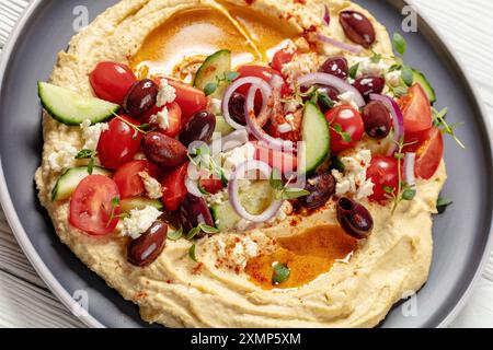 Hummus greco carico di cetrioli freschi, olive, pomodori, feta, cipolle rosse e timo sul piatto, primo piano Foto Stock