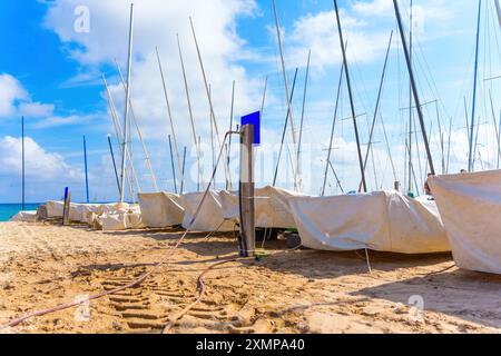 Barche a vela coperte che riposano su una spiaggia sabbiosa con acqua azzurra sullo sfondo a Tarragona, Spagna Foto Stock