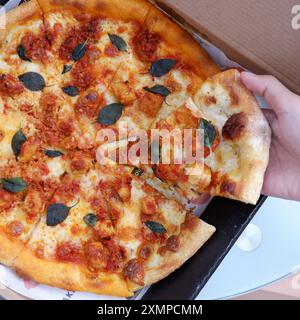 Una giovane signora sta prendendo una fetta di una deliziosa pizza Foto Stock