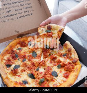 Una giovane signora sta prendendo una fetta di una deliziosa pizza Foto Stock