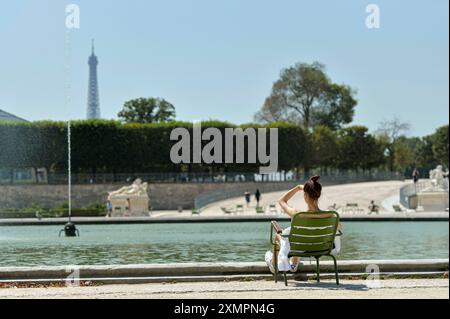 Parigi (Francia): Donna vista da dietro, seduta su una sedia, nel giardino botanico “Jardin des Tuileries”. Donna che si gode il sole davanti a un pon Foto Stock