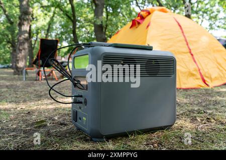 Centrale elettrica portatile con batteria al litio-ferrofosfato che carica i dispositivi elettronici utilizzati in un campo selvaggio, di fronte alla tenda gialla. Portatile Foto Stock