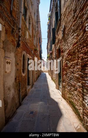 Venezia, Italia - 5 giugno 2024: Stretta strada vuota incorniciata da edifici in mattoni. Foto Stock