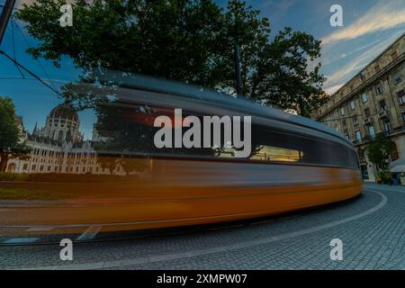 Budapest, Ungheria: 5 luglio 2024: Traffico del tram in Piazza Kossuth Lajos al tramonto. Edificio del Parlamento sulla sinistra. Scatto con esposizione lunga. Foto Stock