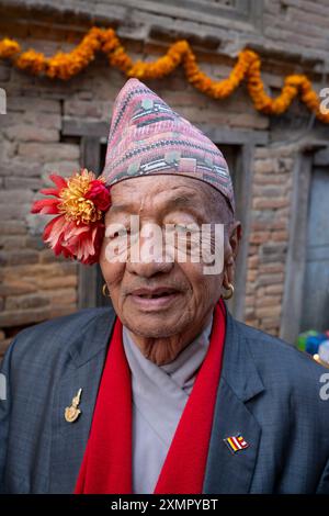 Gentiluomo nepalese che indossa il tradizionale cappello topi dhaka fuori casa, la calendula garland per il festival delle luci Diwali di novembre, Thimi, Kathmandu, Nepal Foto Stock