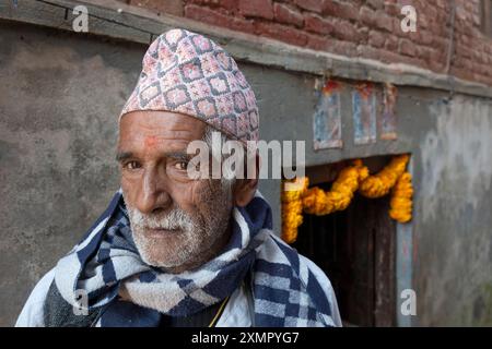 Gentiluomo nepalese che indossa il tradizionale cappello topi di dhaka fuori casa con calendule della ghirlanda per il festival delle luci del Diwali, Thimi, Kathmandu, Nepal Foto Stock