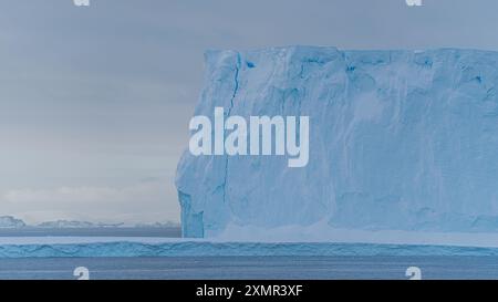 Iceberg Towers Above Us Travel Photography Blue Ice Formation con montagne in lontananza. Vista dalla nave a vela al tramonto in Antartide Foto Stock