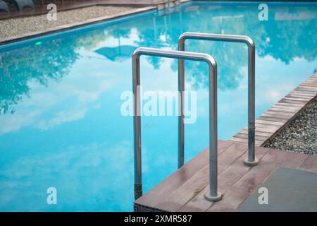 Scala in metallo che conduce ad una piscina blu chiaro con pavimento in legno e ghiaia Foto Stock