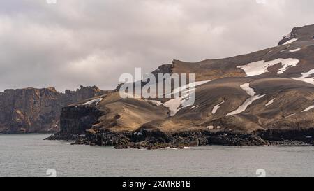 Antartide Deception Island Rugged Cliffs Vista delle patch di neve dalla nave da crociera Ocean. Giorno di sole Fotografia paesaggio natura colonia di pinguini Foto Stock