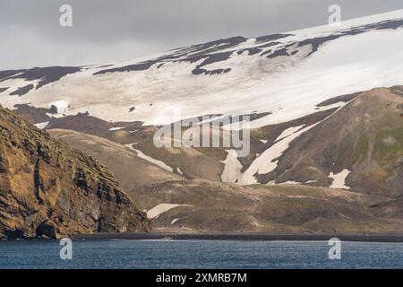 Antartide Penguin Colony Deception Island Rugged Cliffs Snow Covered Glacier View dalla nave da crociera Ocean. Soleggiata giornata paesaggio con ampia vista sulle cime innevate Foto Stock