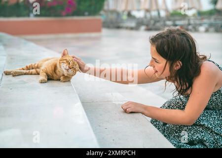 Una ragazza adolescente carina accarezza un gatto di zenzero senzatetto per strada Foto Stock