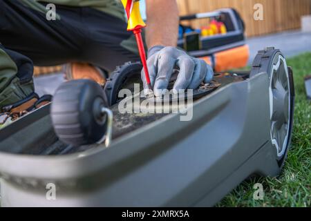 Una persona sta effettuando la manutenzione su un robot rasaerba , utilizzando un cacciavite per ispezionare i suoi componenti. Gli strumenti vengono visualizzati nelle vicinanze in una W organizzata Foto Stock