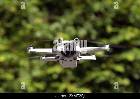 Vista ravvicinata di un piccolo drone non marcato in volo con uno sfondo sfocato di fogliame. Niente persone. Foto Stock