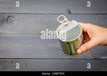 Barattolo di cibo vuoto e aperto in mano, fondo di legno. Foto Stock