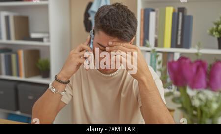 Stressato giovane ispanico che parlava al telefono a casa con mal di testa, mostrando disagio e preoccupazione in un ambiente domestico. Foto Stock