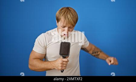 Un giovane biondo con la barba che canta in una spazzola su sfondo blu Foto Stock