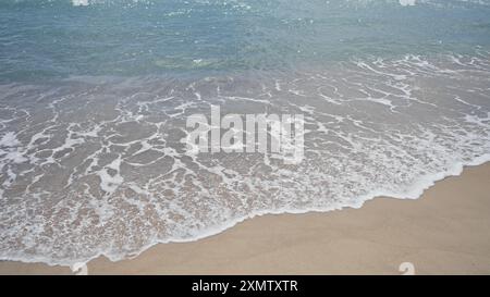 Una tranquilla spiaggia che raffigura dolci onde che si infrangono su una spiaggia sabbiosa sotto un cielo limpido. Foto Stock