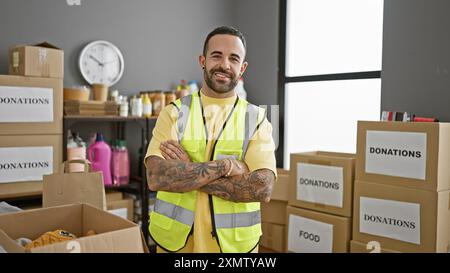 Un uomo ispanico sicuro di sé in un giubbotto ad alta visibilità si trova tra le scatole per donazioni nel magazzino di un'organizzazione di beneficenza. Foto Stock