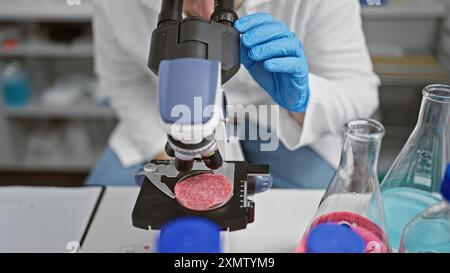 L'uomo caucasico esamina la carne sintetica al microscopio in un moderno laboratorio, ambiente interno. Foto Stock