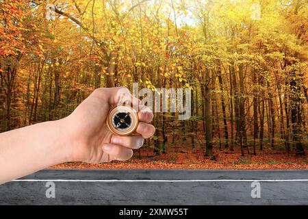 Uomo che tiene la bussola vicino alla strada che attraversa la foresta in autunno, primo piano Foto Stock