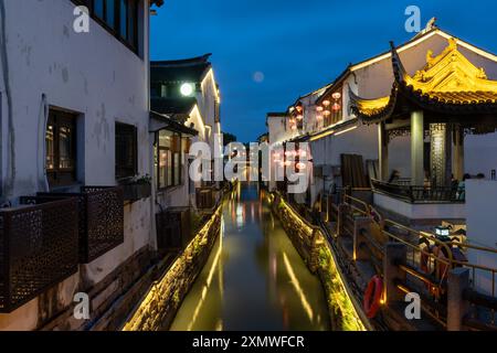 suzhou, Cina - 10 giugno 2024: Uno stretto canale scorre attraverso il cuore di Suzhou, Cina, fiancheggiato da edifici tradizionali illuminati da luci calde. Foto Stock