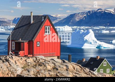 Tipiche case groenlandesi di fronte a iceberg e montagne, soleggiate, estive, Uummannaq, Groenlandia Foto Stock