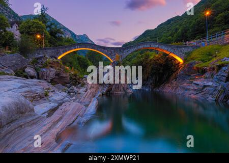 Un'alba estiva sul ponte illuminato Ponte dei salti. Il ponte (chiamato anche "Ponte Romano") si estende lungo il fiume Verzasca a Lavertezzo ed è un trionfo Foto Stock