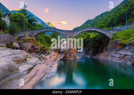 Un'alba estiva sul ponte illuminato Ponte dei salti. Il ponte (chiamato anche "Ponte Romano") si estende lungo il fiume Verzasca a Lavertezzo ed è un trionfo Foto Stock