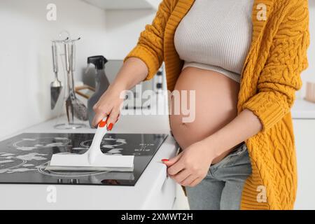 Donna incinta che pulisce la stufa elettrica in cucina Foto Stock