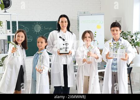 Alunni e insegnanti che tengono microscopio e piante in corso di Biologia a scuola Foto Stock