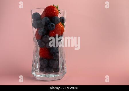 Un bicchiere trasparente è pieno di un variopinto assortimento di fragole e mirtilli, creando una vivace esposizione di prodotti freschi. Foto Stock