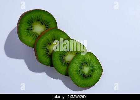 Un gruppo di fette di kiwi disposte una sopra l'altra, che mostrano la polpa verde vibrante e la pelle marrone a contrasto. Foto Stock