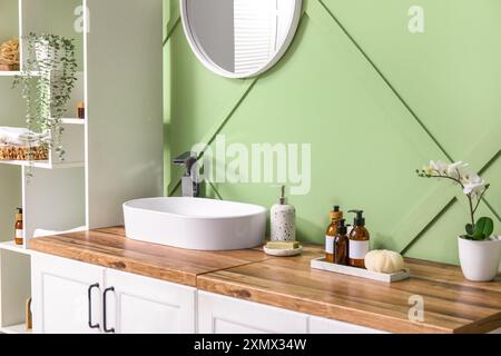 Elegante interno del bagno con scaffalature, cassettiera e lavandino vicino alla parete verde Foto Stock