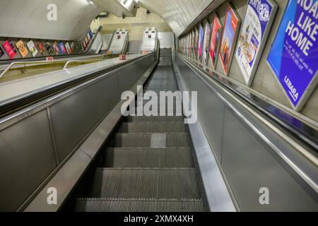 Una scala mobile vuota che scende verso una stazione della metropolitana di Londra, vuota, argentata, isolata Foto Stock