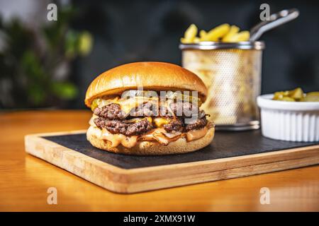 Delizioso hamburger a doppio manzo su ardesia nera con patatine fritte e sottaceti Foto Stock