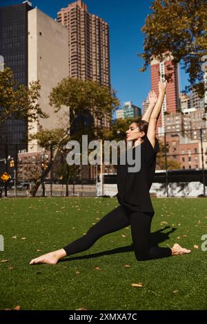 Una giovane donna in abiti neri esegue una graziosa mossa di danza in un campo erboso a New York City. Foto Stock