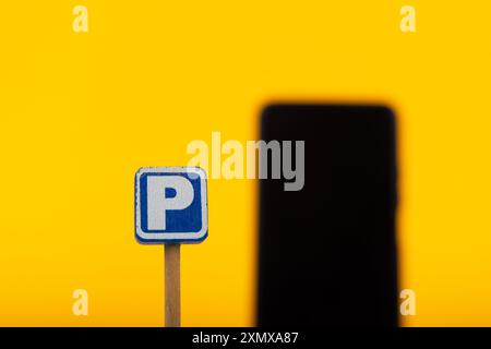 In questa immagine concettuale, un cartello di parcheggio in legno è messo a fuoco con uno smartphone fuori fuoco, su uno sfondo giallo brillante per visua Foto Stock