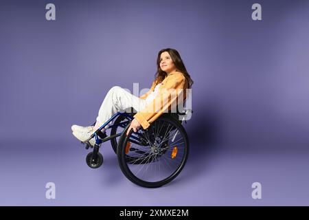 Una giovane donna con un abbigliamento casual, seduta su una sedia a rotelle, guarda attentamente verso l'orizzonte in uno studio di lavanda Foto Stock