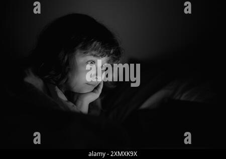 La storia del tempo a letto. Ragazzo che guarda un tablet prima di dormire. Il bambino legge l'e-book. Il bambino guarda lo schermo del tablet in alto. Ragazzo che gioca Foto Stock