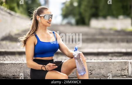 Giovane donna sportiva che beve acqua da una bottiglia dopo essersi allenata al parco. Foto Stock