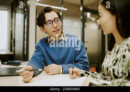 Giovane uomo e donna birazziali moderni che indossa abiti casual eleganti che parlano mentre lavorano insieme in ufficio Foto Stock
