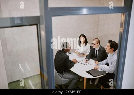 Vista ad alto angolo del giovane candidato afroamericano seduto di fronte a tre manager che hanno un colloquio di lavoro nell'ufficio principale dell'azienda Foto Stock