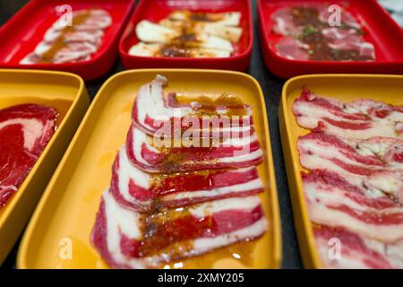 Fette di carne cruda disposte su vassoi gialli e rossi, pronte per essere cotte, molto probabilmente per barbecue o grigliate. Foto Stock