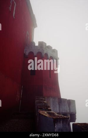 Le pareti rosse intemprate di una torretta al Palácio da pena si stagliano sullo sfondo nebbioso Foto Stock