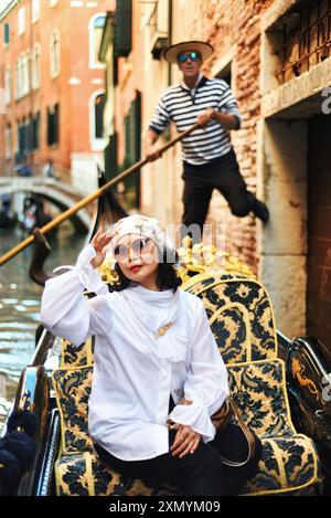 Venezia, Italia, un gondoliere spinge da un muro mentre filtra una donna che cavalca sulla sua gondola lungo un canale veneziano Foto Stock